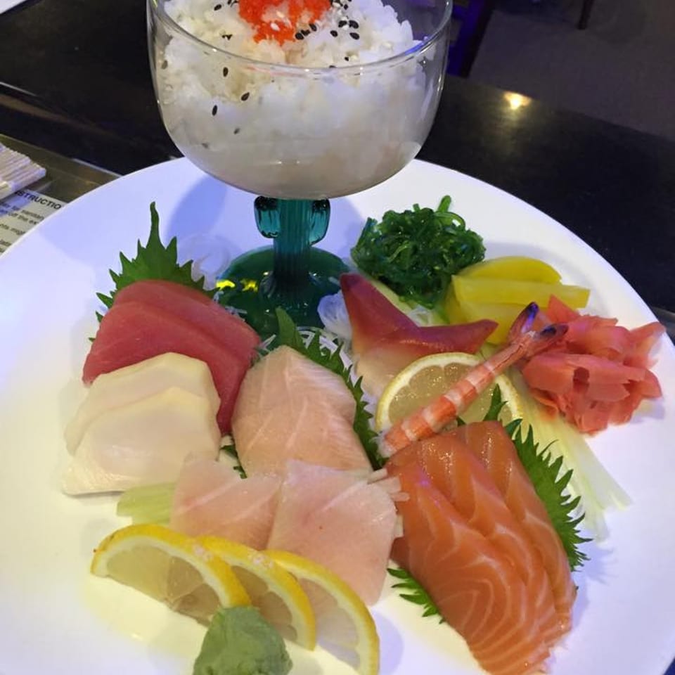A white plate of colorful sashimi, including salmon, tuna, and shrimp, with a side of rice.